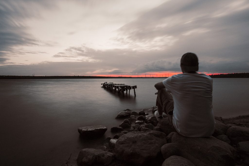 młody mężczyzna kontempluje na jeziorem podczas zachodu słońca
