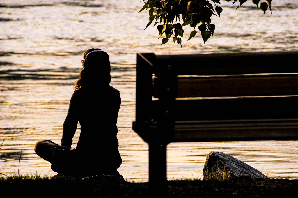 kobieta odwrócona tyłem medytuje na plaży o zachodzie słońca