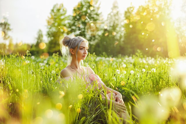 Młoda dziewczyna siedząca na łące pełnej dmuchawców. Wiosenne słońce i wysoka trawa. 
