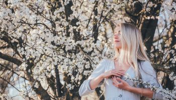 uśmiechnięta kobieta oddycha przy kwitnącym drzewie