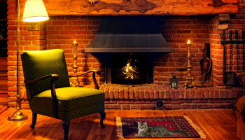 przytulny pokój z palącym się kominkiem, fotelem, kotem i zapalonymi świecami