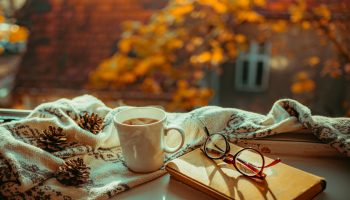 książka, herbata, okulary i koc położone na parapecie, za oknem jesienny krajobraz