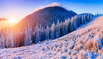Zimowy krajobraz w górach, słońce wychodzące zza góry. Ośnieżone drzewa.