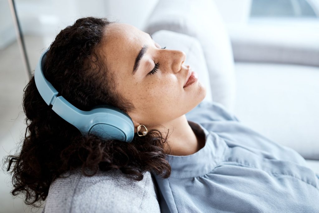 kobieta o czarnych, kręconych włosach ma na uszach duże słuchawki i słucha muzyki 